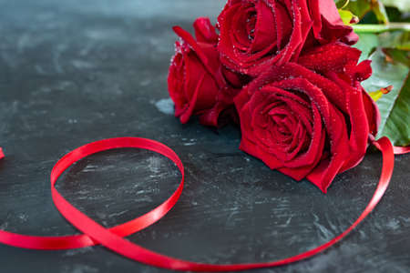 Red roses with ribbon on gray stone slab. Background for romantc valentine's day greetings with short depth of field and space for your textの写真素材
