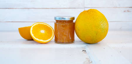 Homemade orange jam in a glass jar with fresh oranges on white wood. Horizontal background for a sweet spread.の写真素材