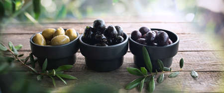 Different varieties of olives on rustic wooden table with branches of an olive tree.の写真素材