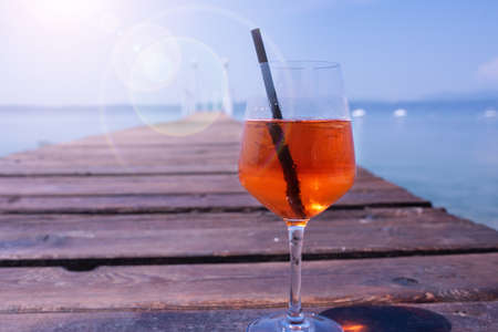 Glass of aperol spritz cocktail by the lake garda. Close up. Holiday background with sun setting on a wooden jetty.の写真素材