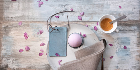 Easter breakfast on gray vintage wood with pink petals. Morning place setting with easter egg and...