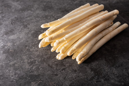 Fresh white asparagus on black background. Seasonal spring vegetables on black stone slab. Sunny kitchen still life for healthy nutrition. Gastronomy background with space for text.の写真素材