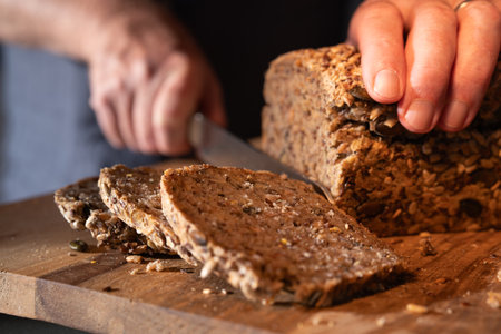 Cutting fresh whole wheat bread into slices on a wooden work surface. Close up.の写真素材