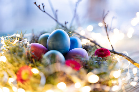 Colorful easter eggs in a herb nest with spring flowers on weathered rustic wooden table. Background...