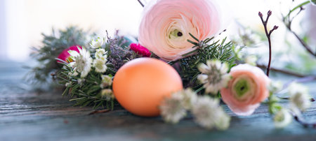 Easter egg in front of a herb nest with spring flowers on weathered rustic wooden table. Close-up...