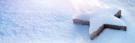 Wooden poinsettia covered with snow in snowy environment. Horizontal background with sun and bokeh for Christmas season. Space for text.の写真素材