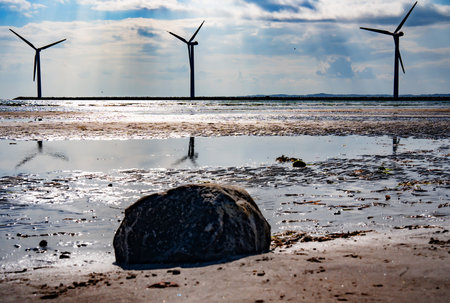 Wind turbine by the sea with glittering sunshine sun and blue sky. Sustainable energy concept. Horizontal background for nature conservation.の写真素材