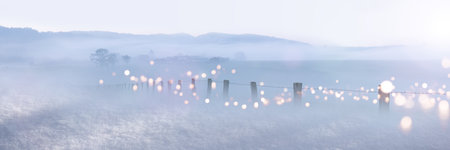 Rural winter panorama in haze with bright bokeh lights. Winter landscape with pasture fence.の写真素材