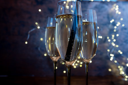 Glasses with champagne in blue light and festive bokeh. Atmospheric new years background for festive moments and space for text. Close up.の写真素材