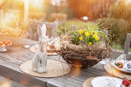 Fresh table set in garden with easter decoration. Easter bunny with spring flowers on wooden table in sunny afternoon.の写真素材