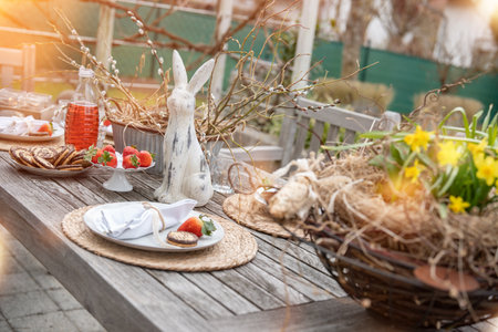 Fresh table set in garden with easter decoration. Easter bunny with spring flowers on wooden table in sunny afternoon.の写真素材