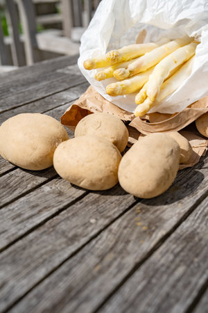 Seasonal white asparagus and potatoes fresh from the market. Healthy vegetables in paper bags on a gray wooden table. Vertical background for local shopping.の写真素材