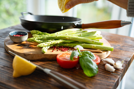 Fresh ingredients for roasted green asparagus. Local vegetables and a cast iron pan on a rustic wooden table. Lemon drops for freshness. Close-up with shallow depth of field.の写真素材