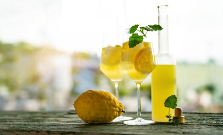 Limoncello liqueur with ice cubes in glasses and a ripe lemon on rustic wooden table.Traditional Italian refreshing summer drink.の写真素材