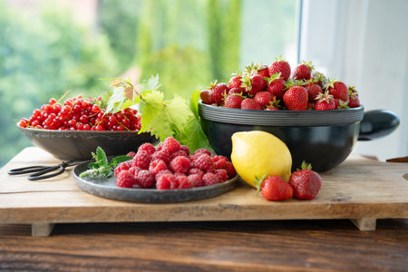 Freshly picked organic summer fruits. Ripe raspberries, strawberries and currants decorated on rustic wood against bright sunny background. Close-up of healthy seasonal fruits.の写真素材