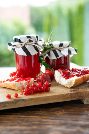 Homemade strawberry and currant jam in jar. Red berries and crusty baguette with fresh fruit spread...