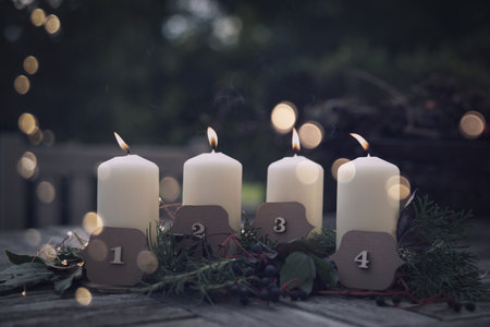 Burning Advent candles with Christmas decorations and golden bokeh on a terrace at dusk. Christmas background with space for text.の写真素材