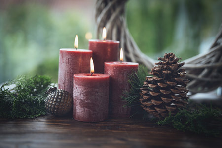 Natural Christmas decoration with four burning red Advent candles. Festive still life on rustic wooden table against green background and space for text.の写真素材