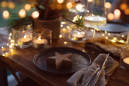 Elegant table decoration for a Christmas dinner. Romantic dinner concept with burning candles in the evening at a restaurant. Close-up with golden bokeh lights. Background for seasonal holiday gastronomy.の写真素材