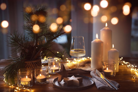 Elegant table decoration for a Christmas dinner. Romantic dinner concept with burning candles in the evening at a restaurant. Close-up with golden bokeh lights. Background for seasonal holiday gastronomy.の写真素材