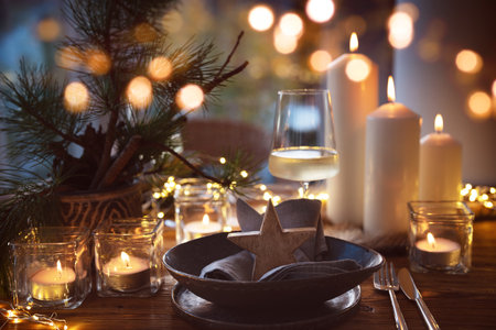Elegant table decoration for a Christmas dinner. Romantic dinner concept with burning candles in the evening at a restaurant. Close-up with golden bokeh lights. Background for seasonal holiday gastronomy.の写真素材