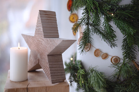 Natural Christmas decoration with garland made of fir branches and lit candle in front of white pillar.の写真素材