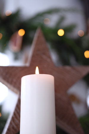 Burning white candle with wooden poinsettia in front of natural Christmas decoration. Vertical Christmas background with short depth of field. Close up.の写真素材
