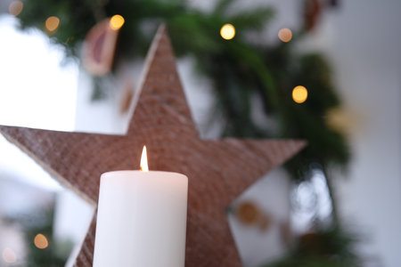 Burning white candle with wooden poinsettia in front of natural Christmas decoration. Christmas background with short depth of field. Close up.の写真素材