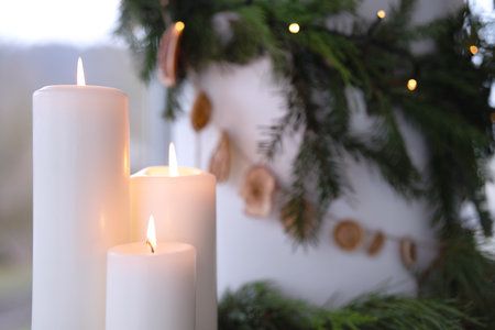 Three burning white candles with natural Christmas decoration in the background and short depth of field.の写真素材