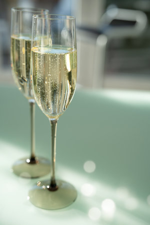 Two filled champagne glasses on a modern glass table. Elegant modern style with soft bright green background and light bokeh. Vertical close-up.の写真素材