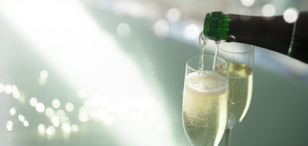Pouring champagne into glasses. Bottle of sparkling wine against an elegant, modern light green background with a soft bokeh. Celebrating with flowing golden drink.の写真素材