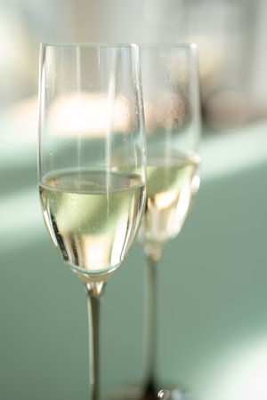 Two filled champagne glasses on a modern glass table. Elegant modern style with soft bright green background and light bokeh. Vertical close-up.の写真素材