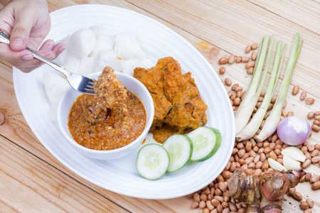 Chicken Rendang is popular dishes in Malaysia, with onion, peanut and lemongrass as decoration on wooden tableの写真素材