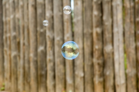 Flying soap bubbles reflecting wooden fence on the background