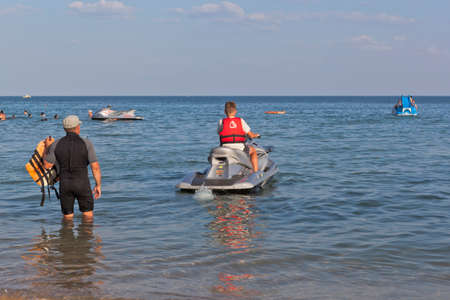 village Zaozernoe, Evpatoria, Crimea, Russia - July 18, 2021: A boy under the supervision of an instructor drives off on a jet ski from the Super Aqua beach in the resort village of Zaozernoye, Evpatoria, Crimeaのeditorial素材