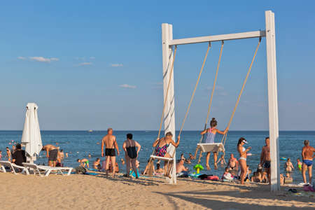Zaozernoe, Saksky district, Crimea, Russia - July 18, 2021: Vacationers swing on a swing on the Super Aqua beach in the resort village of Zaozernoye, Saksky district, Evpatoria, Crimeaのeditorial素材