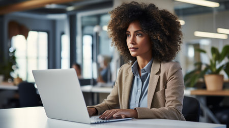 Beautiful Middle Eastern Manager Sitting at a Desk in Creative Office. Young Stylish Female with Curly Hair Using Laptopの素材