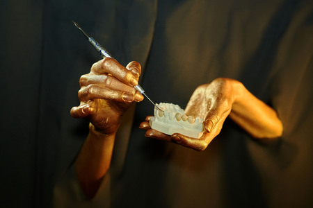two golden hands with a dental instrument on a black backgroundの写真素材