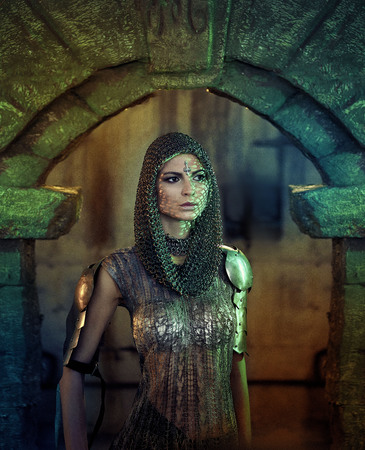 A beautiful warrior girl with a sword and in armor. A model in a chain skirt and a vest in a mysterious plase. Fantasy photo.の写真素材