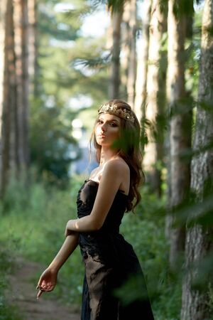 young, beautiful girl in a black dress with a crown in the forestの写真素材