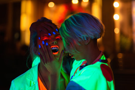 two girls in ultraviolet clothes pants and t-shirts posing in the night city