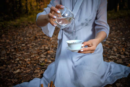 A girl in a blue kimono sits in the autumn forest and prepares teaの写真素材