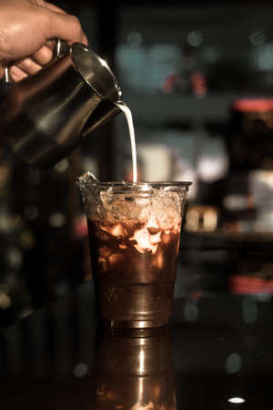 Barista pouring milk into a glass of iced coffeeの写真素材