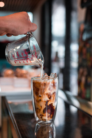 Barista pouring milk into a glass of iced coffeeの写真素材