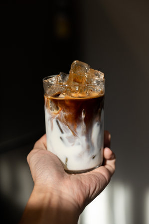Iced coffee in a glass with ice cubes in hand on dark backgroundの写真素材