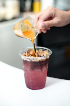 Barista pouring milk into a glass of iced americano coffee