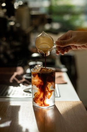 Barista pouring coffee in a glass with ice cubes on the tableの写真素材