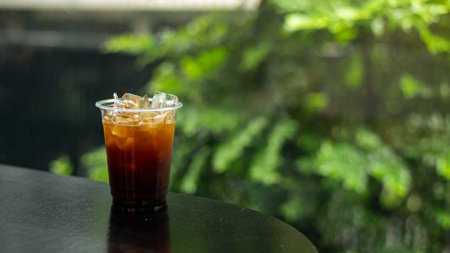 Ice coffee in a glass on the table with green nature background.