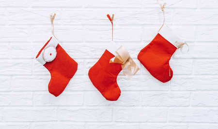Red and white christmas stockings hanging from a clothesline against a white brick wall background holidayの写真素材