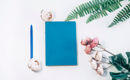 top view of office desk table with digital camera and blue notepad on white background, decorated...